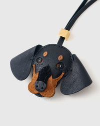 Close-up of handmade Dachshund leather bag charm — hand-stitched visible edges on French Alran goatskin, hand-layered black-and-tan markings. STICKYZOO Amsterdam design.