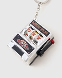 Close-up of playable miniature chrome slot machine charm showing triple sevens, fruit symbols, and red pull lever attached to stainless steel chain