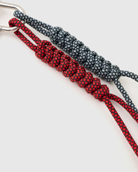 Close-up of red and charcoal gray hand-knotted paracord ropes with intricate braiding pattern and stainless steel clasp connection