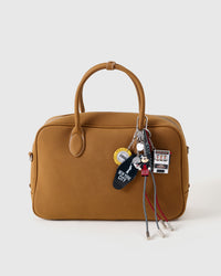Lucky Slot Stack Charm clipped onto a tan leather handbag showing mini slot machine, character figure, casino chip, NYC tag, and braided paracord ropes hanging from the handle