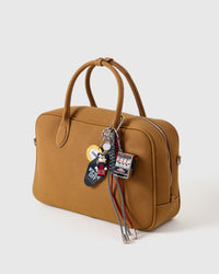 Lucky Slot Stack Charm on tan handbag from three-quarter angle showing slot machine, tuxedo character figure, NYC motel tag, and casino chip with paracord rope tassels