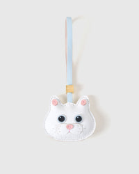 White British Shorthair cat charm handmade from French Alran genuine goatskin — pure ivory body, pink inner ears, dark eyes, pink nose, light-blue leather strap. Three days by hand. Arrives in luxury gift packaging. Designed in Amsterdam.
