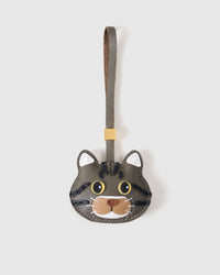 American Shorthair cat charm in the cool gray-olive tabby edition — deep olive body, bold black stripes, yellow eyes, white chin, olive-grey leather strap. Hand-cut from real French leather over three days.