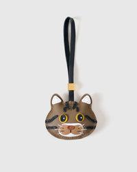 Brown tabby American Shorthair cat charm handmade from French Alran genuine goatskin — warm chestnut body, bold black stripes, yellow eyes, white chin, caramel muzzle, black leather strap. Three days by hand. Arrives in luxury gift packaging. Designed in Amsterdam.
