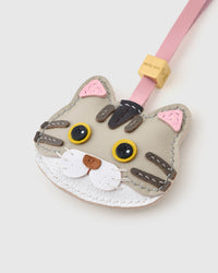 Tight close-up of the silver-tabby British Shorthair face — pink inner ears, yellow eyes in real leather, darker tabby stripes hand-stitched across the forehead. Every panel by hand.