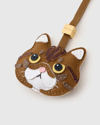 Tight close-up of the Exotic Shorthair face — amber eyes in real leather, chestnut tabby forehead, pink nose, white chin. Every panel by hand.