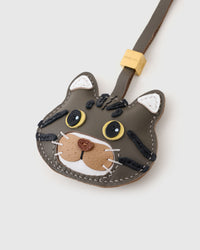 Tight close-up of the gray-olive American Shorthair face — yellow eyes in real leather, bold black stripes across the olive forehead, caramel muzzle. Every panel by hand.