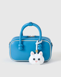 White British Shorthair styled on a vivid blue box bag, front — the small specific piece that makes the bag feel personal.