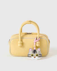 Silver-tabby British Shorthair styled on a pastel-yellow box bag, front angle — the small piece that makes a simple bag feel personal.