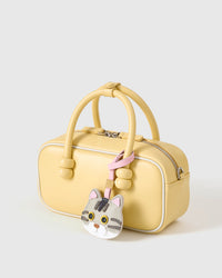 Silver-tabby British Shorthair on a pastel-yellow box bag, side angle — real French leather, 3 days by hand.