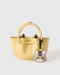 The silver Maine Coon charm styled on a soft-yellow bucket bag — the small piece that makes a simple bag feel personal.