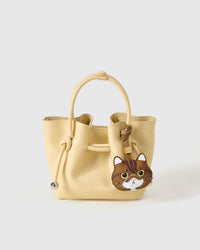 Exotic Shorthair styled on a soft-yellow bucket bag, front — the small piece that turns a simple bag into a personal one.