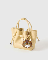 Exotic Shorthair on a soft-yellow bucket bag, side angle — Real French leather, 3 days by hand.