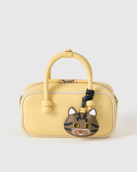 Brown tabby American Shorthair styled on a pastel-yellow box bag, front — the small piece that turns a simple bag into a personal one.