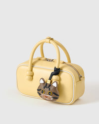 Brown tabby American Shorthair on a pastel-yellow box bag, front angle — real French leather, 3 days by hand.