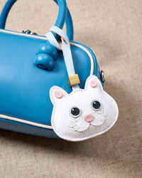 White British Shorthair hanging on a vivid blue box bag, side angle — Real French leather, 3 days by hand.