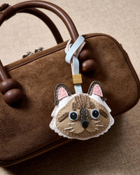 Both editions of the point-color Ragdoll charm side by side — leather strap loop for bags, or 18K gold-plated keychain clip with engraved STICKYZOO disc.