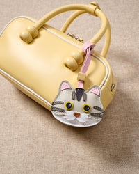 Silver-tabby British Shorthair on a pastel-yellow box bag, side angle — loved by thousands of British Shorthair people. Real French leather, 3 days by hand.