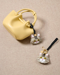 Silver Maine Coon charm in both strap and keychain editions, styled with a yellow bucket bag. Loved by thousands of cat lovers — real French leather + suede, 3 days by hand.