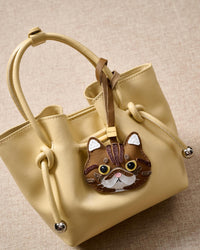 Exotic Shorthair on a soft-yellow bucket bag, side angle — rated 4.9★ by thousands of buyers. Real French Alran leather, 3 days by hand.
