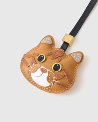 Tight close-up of the ginger British Shorthair face — silver-tipped ears, yellow eyes in real leather, tabby stripes hand-stitched across the forehead. Every panel by hand.