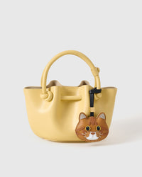Ginger British Shorthair styled on a pastel-yellow bucket bag, front — real French leather, made to be carried on the bag that sees every day.