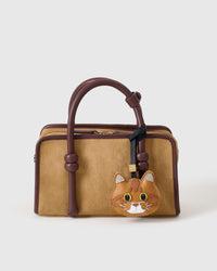 Ginger British Shorthair charm styled on a tan suede top-handle bag, front angle — the small piece that turns a simple bag into a personal one.