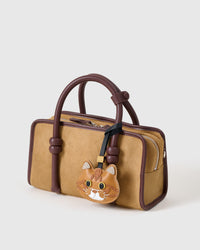 Ginger British Shorthair on a tan suede top-handle bag, side angle — 5,000+ reviews across STICKYZOO. Real French leather, 3 days by hand.