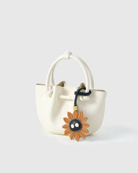 STICKYZOO Sunflower Mood Charm clipped to a handbag — handmade French Alran goatskin in caramel with dark character centre. 3-day artisan build.