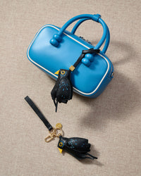 Blackbird charm styled on a bag, front — a small, specific piece that turns a simple bag into a personal one.