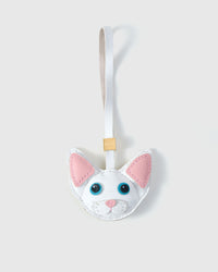 Pure-white Devon Rex cat charm — white body, pink inner ears, blue eyes, pink nose, white leather strap. Hand-cut from real French Alran goatskin over three days. Arrives in luxury gift packaging.