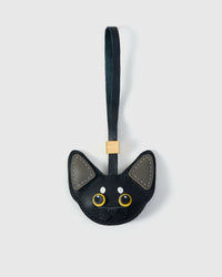 All-black Devon Rex cat charm with grey ears — black body, grey ears, gold-yellow eyes, black leather strap. Hand-cut from real French Alran goatskin over three days. Arrives in luxury gift packaging.