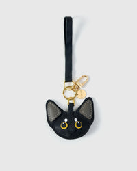 The Devon Rex cat charm — available in taupe, snow white, black-and-white, and black-and-grey editions. Hand-cut French Alran goatskin, 3 days per piece, finished by hand.