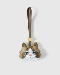 Classic Ragdoll cat charm handmade from French Alran genuine goatskin — cream body, tan-brown markings, vivid blue eyes, pink nose, white face mask, taupe leather strap. Three days by hand. Arrives in luxury gift packaging. Designed in Amsterdam.
