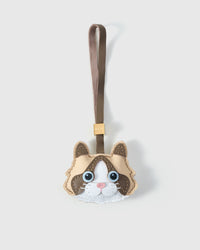 Cream Ragdoll cat charm handmade from French Alran genuine goatskin — pale cream body, deep brown markings, blue eyes, pink nose, taupe leather strap. Three days by hand. Arrives in luxury gift packaging. Designed in Amsterdam.