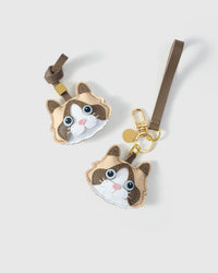 Both editions of the Cream Ragdoll side by side — leather strap loop for bags, or 18K gold-plated keychain clip.