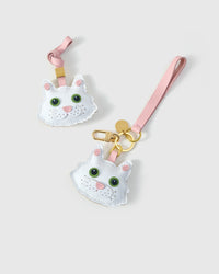 Both editions of the white Maine Coon side by side — leather strap loop for bags, or 18K gold-plated keychain clip.