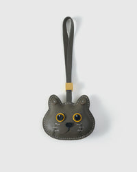 Blue British Shorthair cat charm handmade from French Alran genuine goatskin — soft blue-grey body, gold eyes, small dark nose, olive-grey leather strap. Three days by hand. Arrives in luxury gift packaging. Designed in Amsterdam.