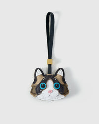 Ragdoll cat charm handmade from French Alran genuine goatskin — bicolour caramel and brown body, white face mask, vivid blue eyes, pink nose, black leather strap. Three days by hand. Arrives in luxury gift packaging. Designed in Amsterdam.