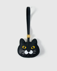 Chubby Midnight British Shorthair cat charm handmade from French Alran genuine goatskin — pure black body, wide gold eyes, white whisker-pad accents, small dark nose, black leather strap. Three days by hand. Arrives in luxury gift packaging. Designed in Amsterdam.