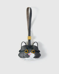Close-up of the long-hair tabby cat charm face — gold-yellow eyes in real leather, hand-stitched tabby stripes, real fiber whiskers. Every panel by hand.