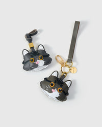 Both editions of the gray-and-white long-hair tabby — leather strap loop for bags, or 18K gold-plated keychain clip with engraved STICKYZOO disc.