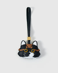 Gray-and-white long-hair tabby cat charm — gray body, white face mask and chin, gold-yellow eyes, pink nose, real fiber whiskers, olive-grey leather strap. Hand-cut from real French Alran goatskin over three days.
