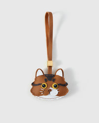 Orange long-hair tabby cat charm — caramel body, brown forehead stripes, gold-yellow eyes, white inner ears and chin, real fiber whiskers, tan leather strap. Hand-cut from real French Alran goatskin over three days.