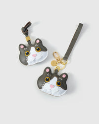 Both Grey Muse editions of the British Shorthair side by side — leather strap loop for bags, or 18K gold-plated keychain clip.