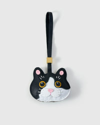 Black Muse British Shorthair charm — black face and ears with white face mask, gold-orange eyes, pink inner ears, pink nose, black leather strap. Hand-cut from real French Alran goatskin over three days.
