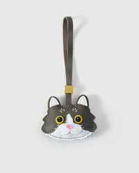 Gray European Shorthair cat charm handmade from French Alran genuine goatskin — soft gray body, white face mask, gold-yellow eyes, pink nose, olive-grey leather strap. Three days by hand. Arrives in luxury gift packaging. Designed in Amsterdam.