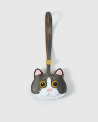 Grey mist British Shorthair cat charm — grey body, white face mask, gold eyes, pink nose, olive-grey leather strap. Hand-cut from real French Alran goatskin over three days.