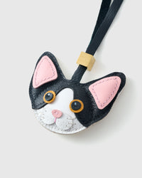 Close-up of the black-and-white Devon Rex cat charm — pink inner ears, gold-orange eyes in real leather, white face mask. Every panel by hand.