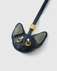Close-up of the all-black Devon Rex cat charm with grey ears — gold-yellow eyes in real leather, every panel by hand.